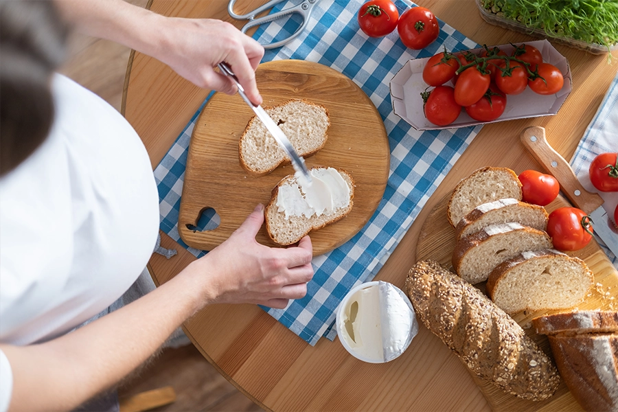 A pregnant young woman spreads curd cheese on slices of bread.